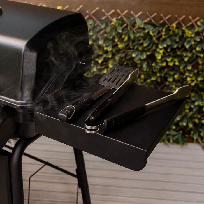 Black outdoor grill with smoking lid and attached tools on side tray.