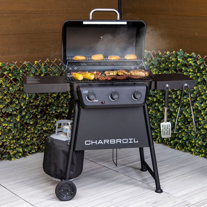 Black Char-Broil gas grill with food cooking, side shelves, and tools.