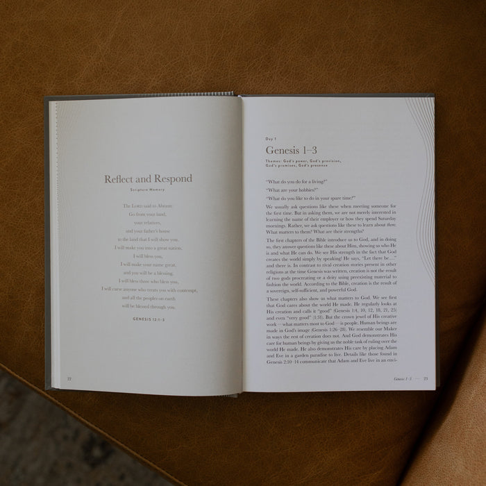A Year in the Bible Hardcover opened to the Genesis Reflect and respond page on a leather couch