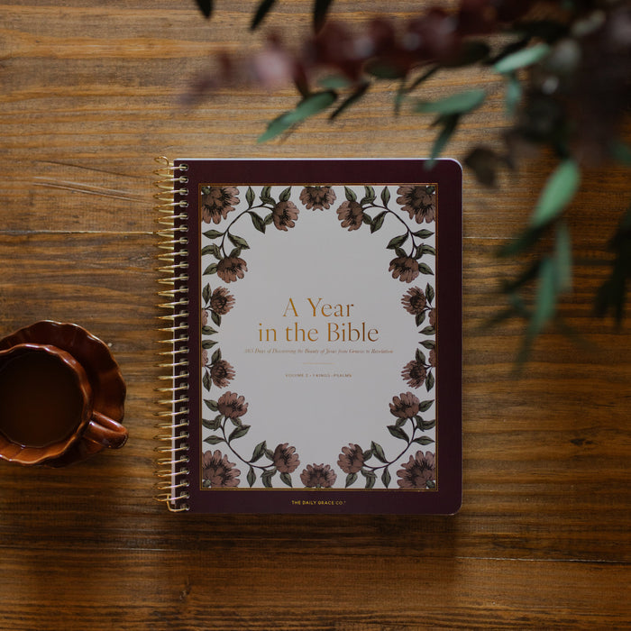 A Year in the Bible Spiral next to a brown coffee cup on a brown wooden table