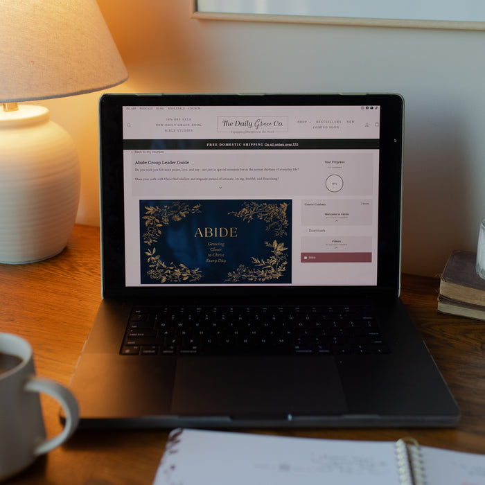 Laptop on a desk with a website open on the screen, next to a cup of coffee and a lamp.