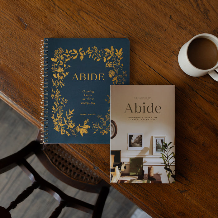Two books titled 'Abide' on a wooden table with a cup of coffee.