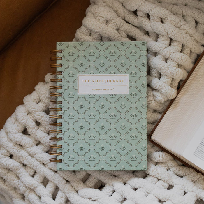 Abide Journal Refresh Cover on a white knitted blanket next to an open bible on a leather couch