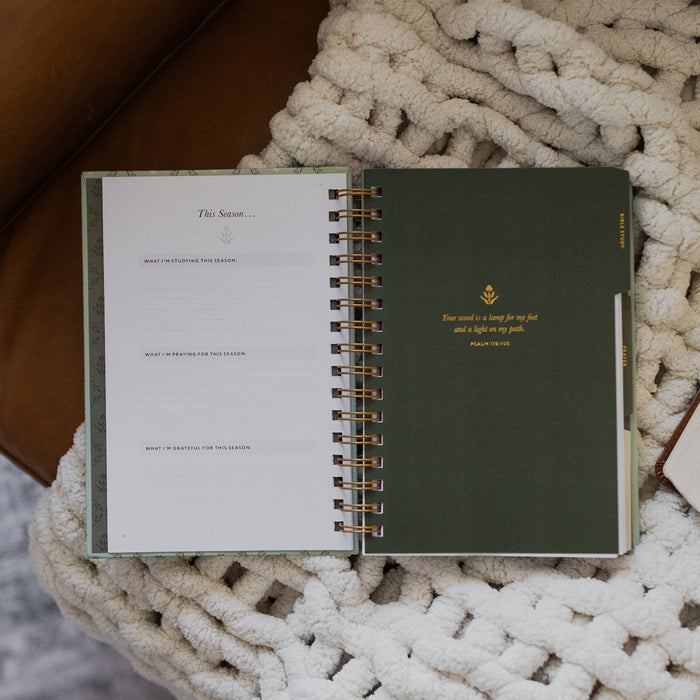 Abide Journal Refresh opened to the bible study section on a white knitted blanket on a leather couch