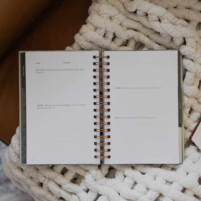 Abide Journal Refresh opened to the prayer section on a white knitted blanket on a leather couch