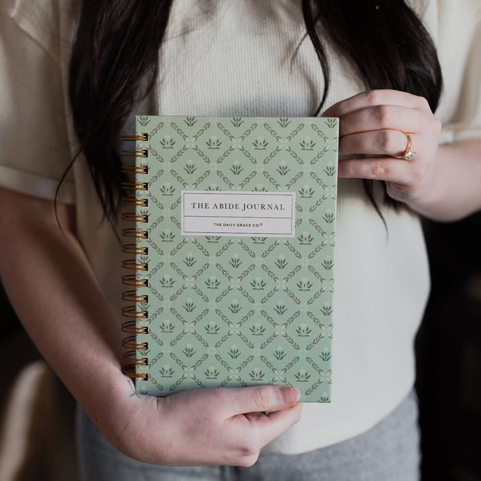 A woman with black hair holding The Abide Journal Refresh from the bottom of the journal.