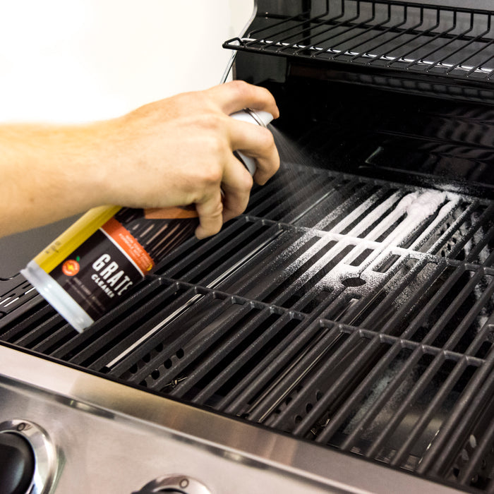 White spray can labeled "Grate Cleaner" being used on a black grill grate.