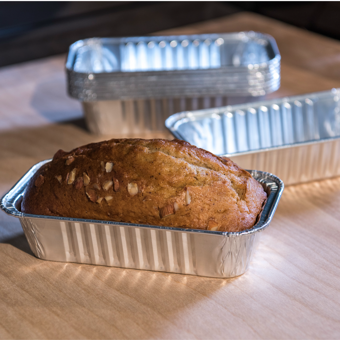 Golden loaf cake in aluminum pan with nuts, on wooden surface.