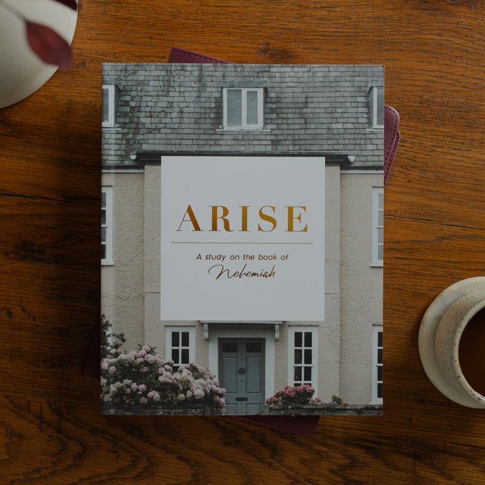 Book titled 'Arise' on a wooden table with a cup of coffee and flowers.
