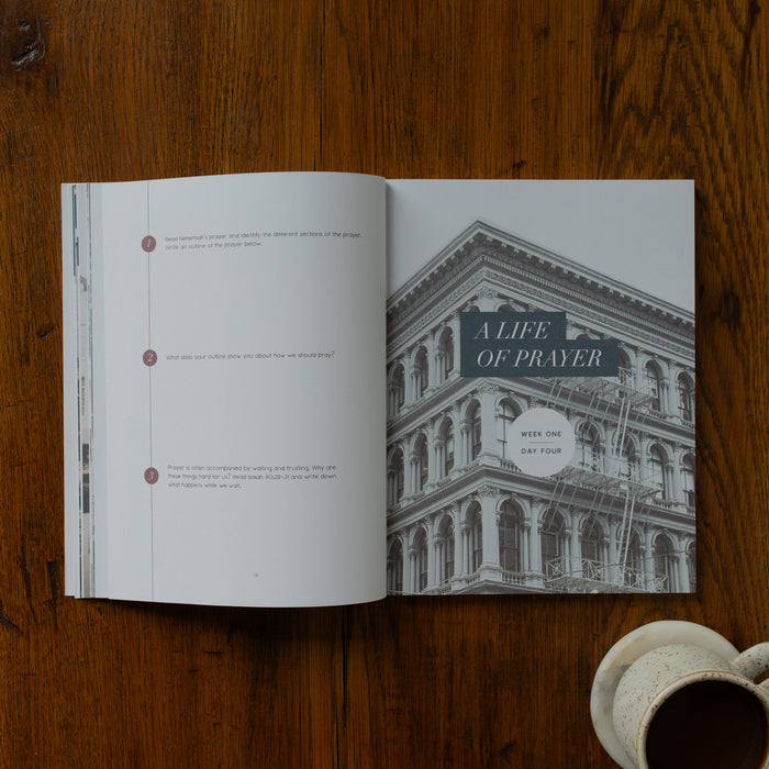 Open book on a wooden surface with a building illustration and 'Alife of Prayer' text.