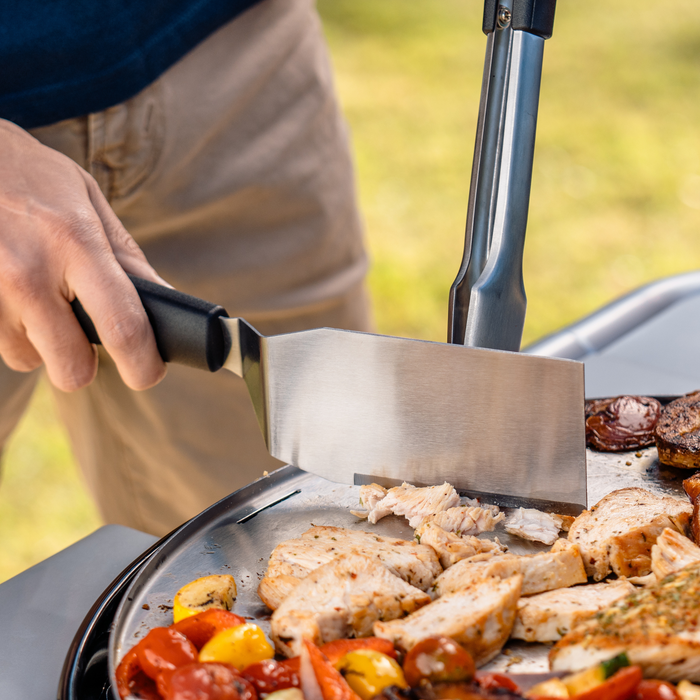 Black-handled kitchen knife slicing grilled chicken on a pan.