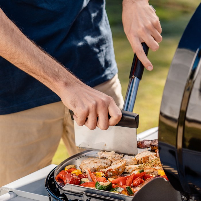 Black-handled kitchen knife cutting grilled chicken and vegetables on a barbecue.