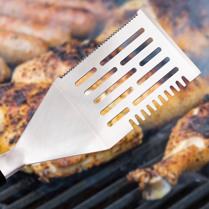 Silver grill spatula with slotted design, ideal for grilling chicken.