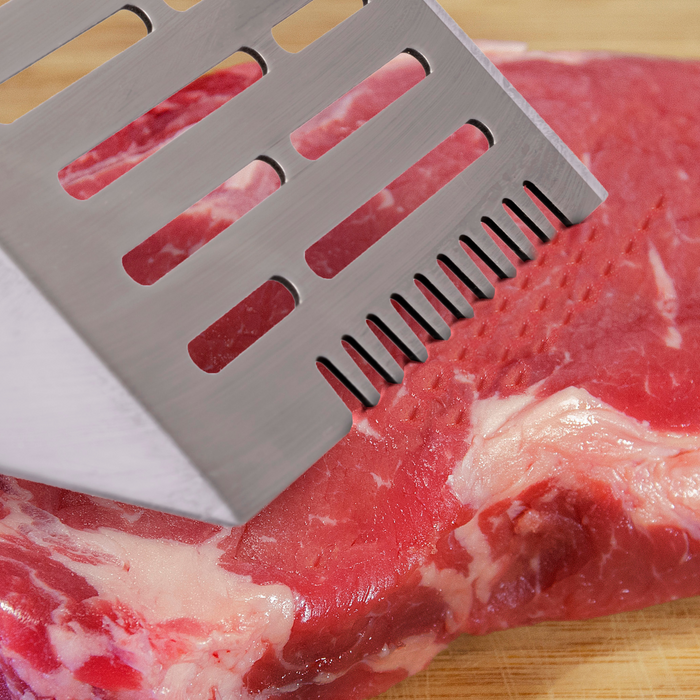 Silver perforated meat tenderizer on raw beef.