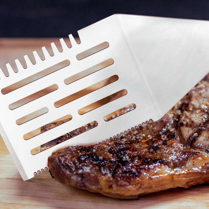 White plastic spatula with slotted design, lifting cooked meat.