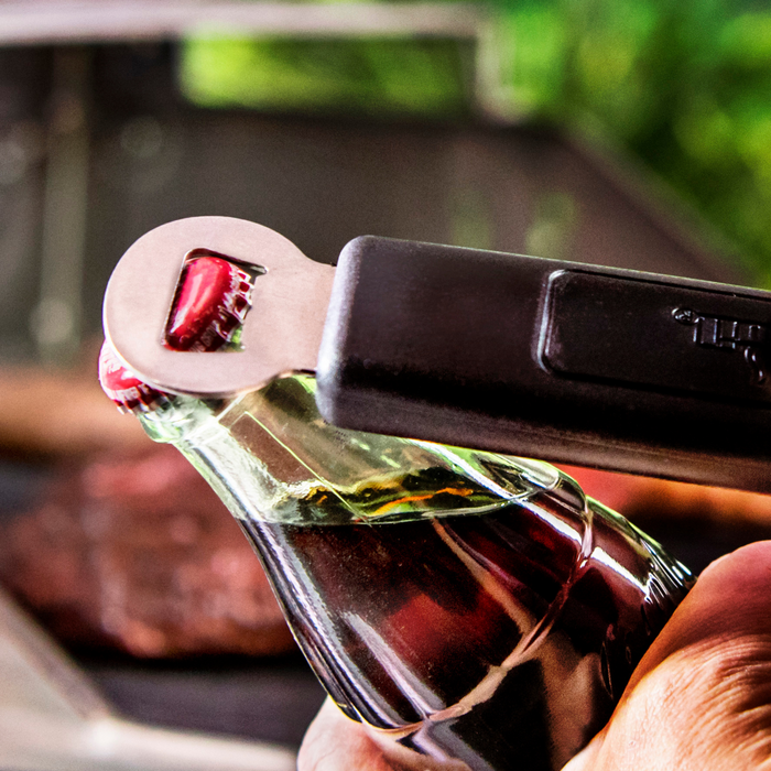 Red Coca-Cola bottle being opened with a black bottle opener.
