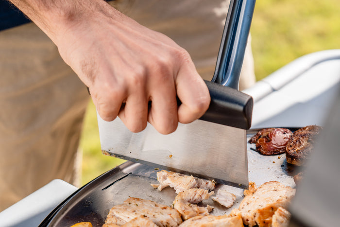 Black-handled knife slicing cooked chicken on a grill.