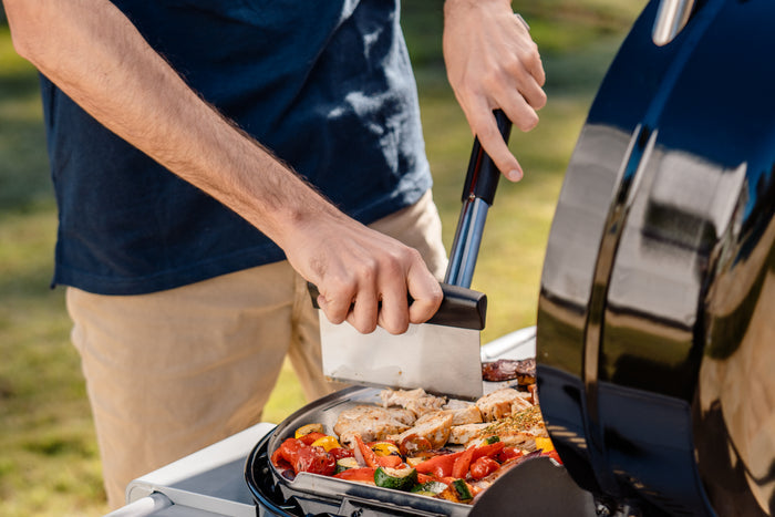 Portable black grill with vegetables and meat cooking outdoors.