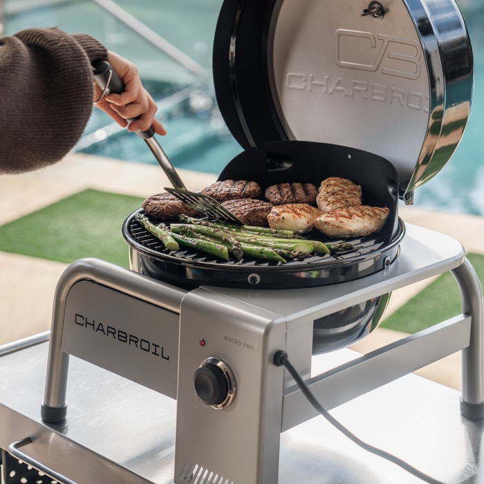 Silver Char-Broil Bistro Pro electric grill with charcoal mode, cooking burgers, chicken, and asparagus.