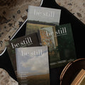 Be Still magazines stacked on one another on a black table