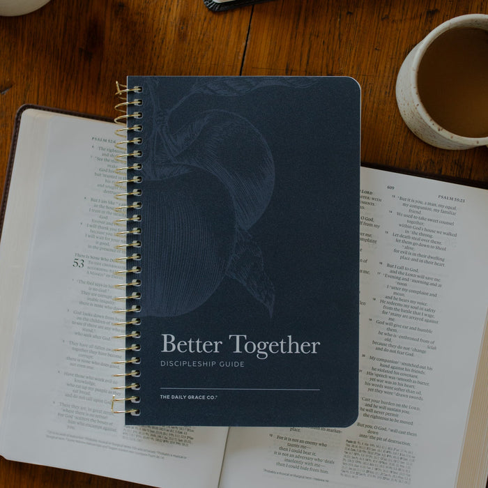 The Better Together Discipleship Guide on an open bible on a wooden table near a white coffee cup