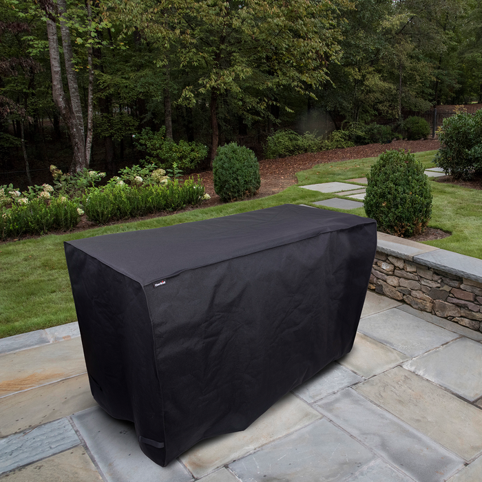 Black outdoor grill cover on patio with stone steps and greenery.