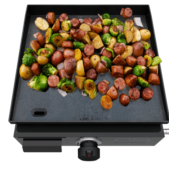 Black Char-Broil griddle with sausages, potatoes, and Brussels sprouts cooking.