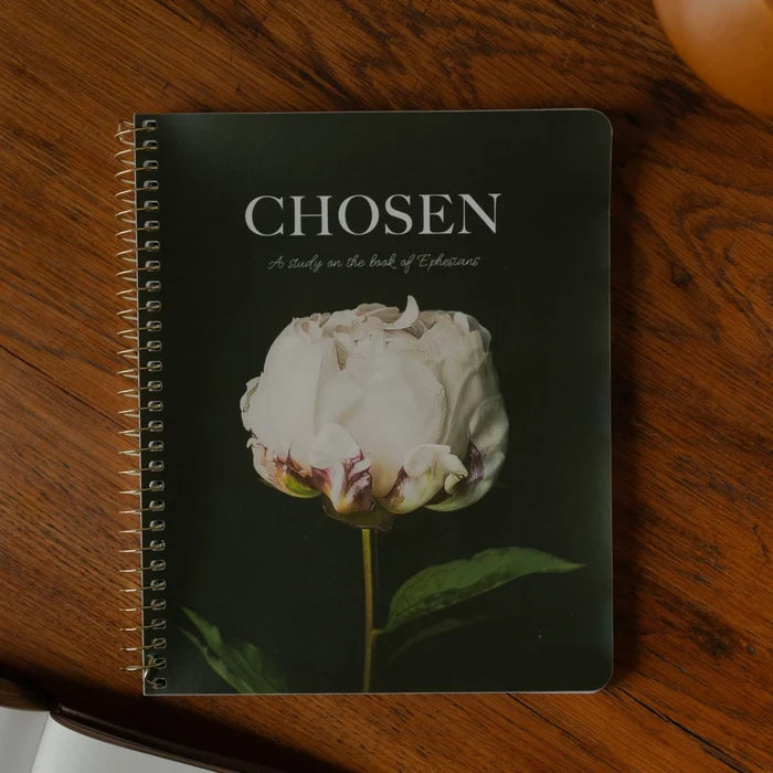 Spiral labeled Chosen with a white rose on the cover on a wooden table next to an open bible