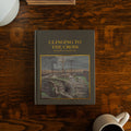 Clinging to the Cross Spiral hardcover cover on a wooden table next to a coffee cup