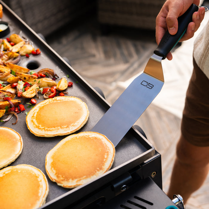 CB brand knife with black handle, used for cooking pancakes and vegetables on a griddle.