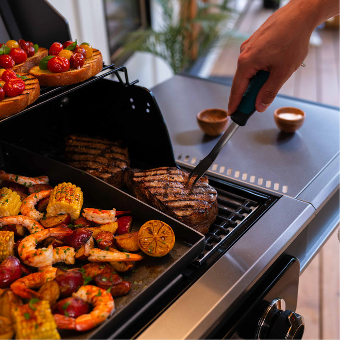 Electric grill with black surface, cooking steak, shrimp, corn, and vegetables.