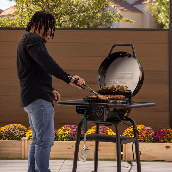 Black Char-Broil Bistro Pro electric grill with charcoal mode, cooking steaks and vegetables.