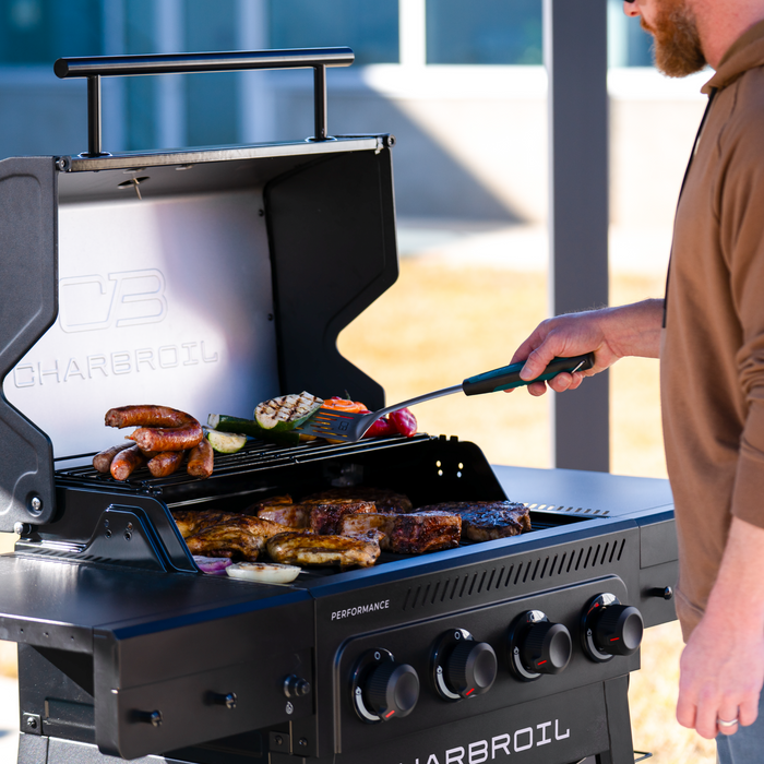 Black Char-Broil Performance gas grill with steaks, sausages, and vegetables cooking.