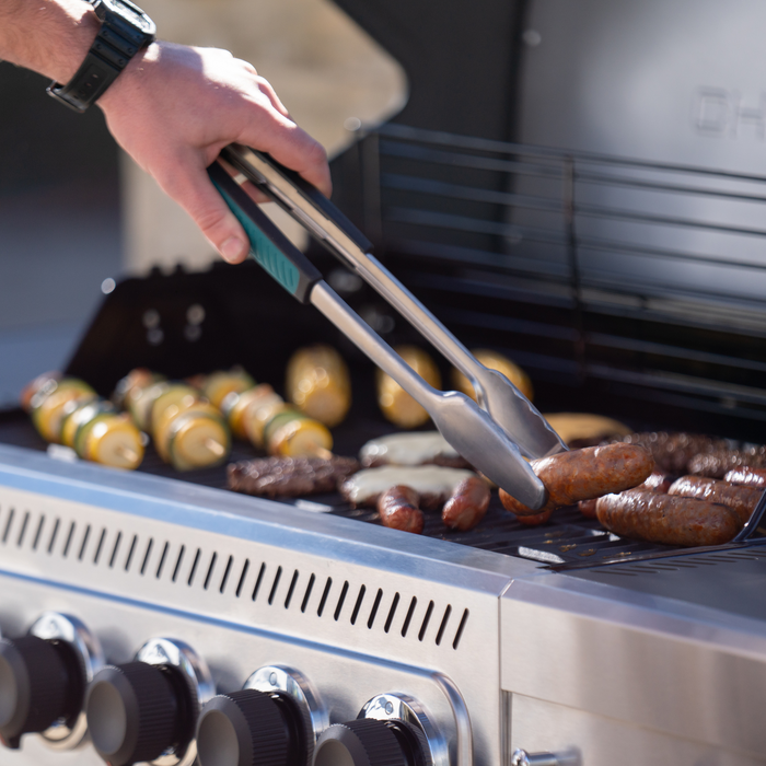 Silver tongs with teal handles used for grilling sausages and kebabs on a barbecue.
