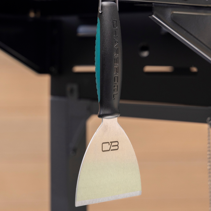Black and teal-handled scraper with "CB" logo on blade, hanging in kitchen.
