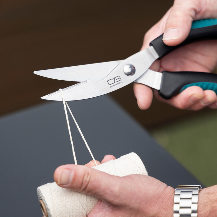 Black-handled scissors cutting white string, Char-Broil brand.