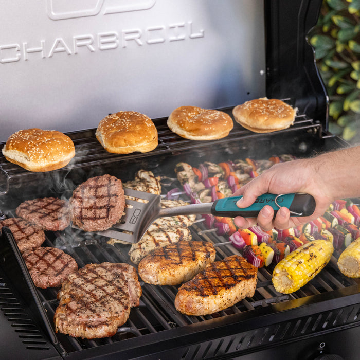Hand using a spatula to grill burgers, chicken, corn, kebabs, and buns on a Char-Broil barbecue grill.