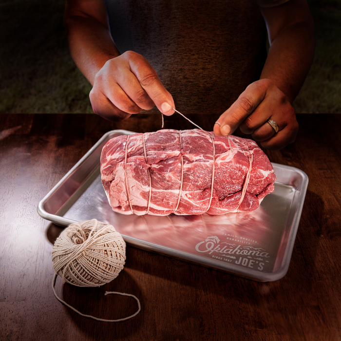 Red meat tied with string on a tray, prepared for cooking.