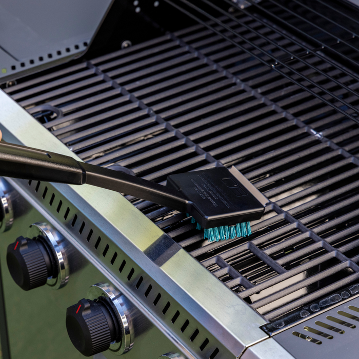 Black grill brush with green bristles on a black grill grate.