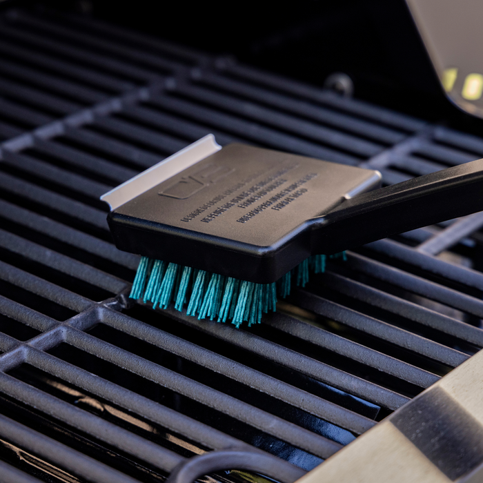 Black grill brush with teal bristles and metal handle, cleaning grill grates.