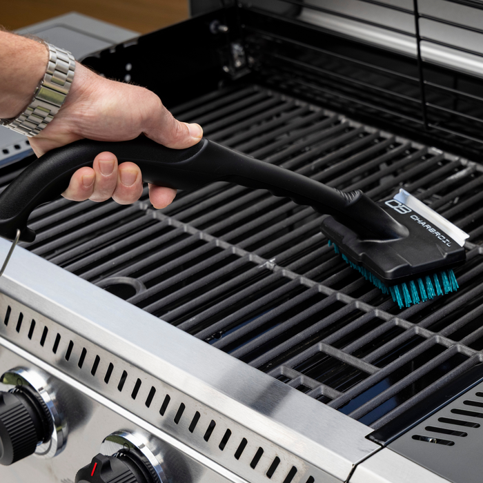 Black Char-Broil grill brush with teal bristles, cleaning a grill.