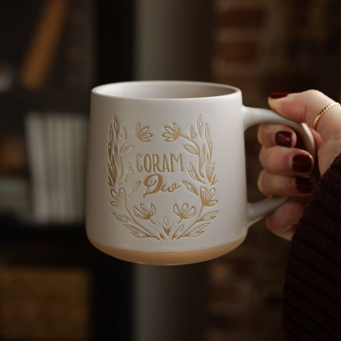 A woman holding a coffee cup with the words Corum Deo on it