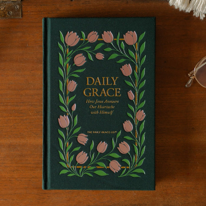 The Daily Grace Hardcover book cover on a wooden desk near a pair of glasses