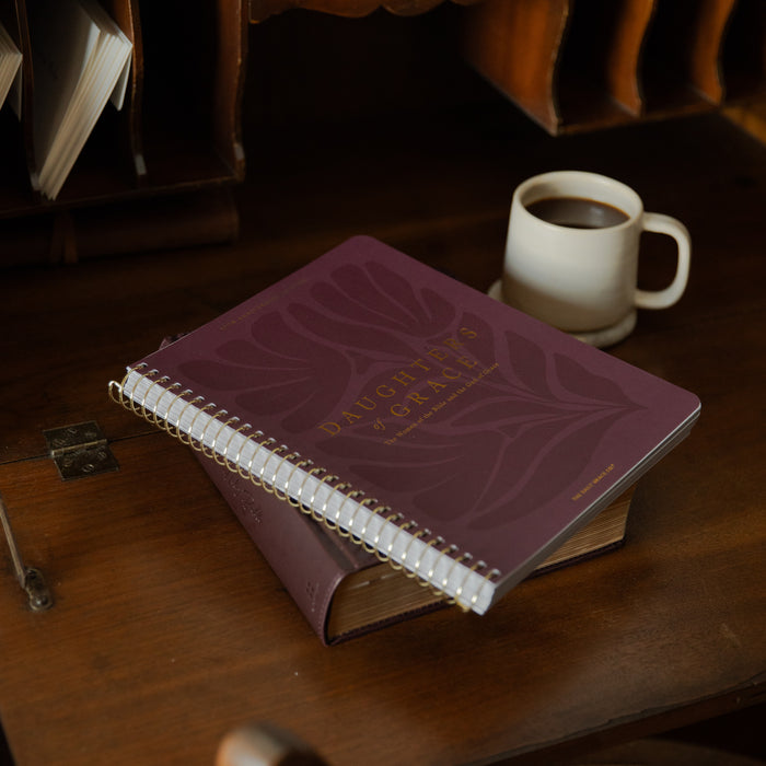 Purple Bible Study with white pages on a wooden table next to a cup of coffee.