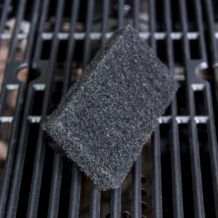 Gray abrasive cleaning pad on black grill grates.