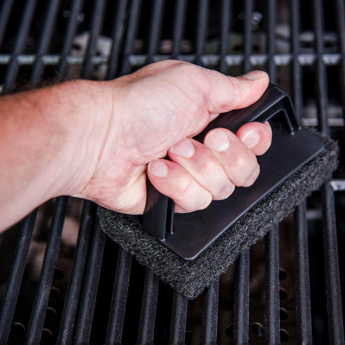 Black grill cleaning brush with foam pad and handle.