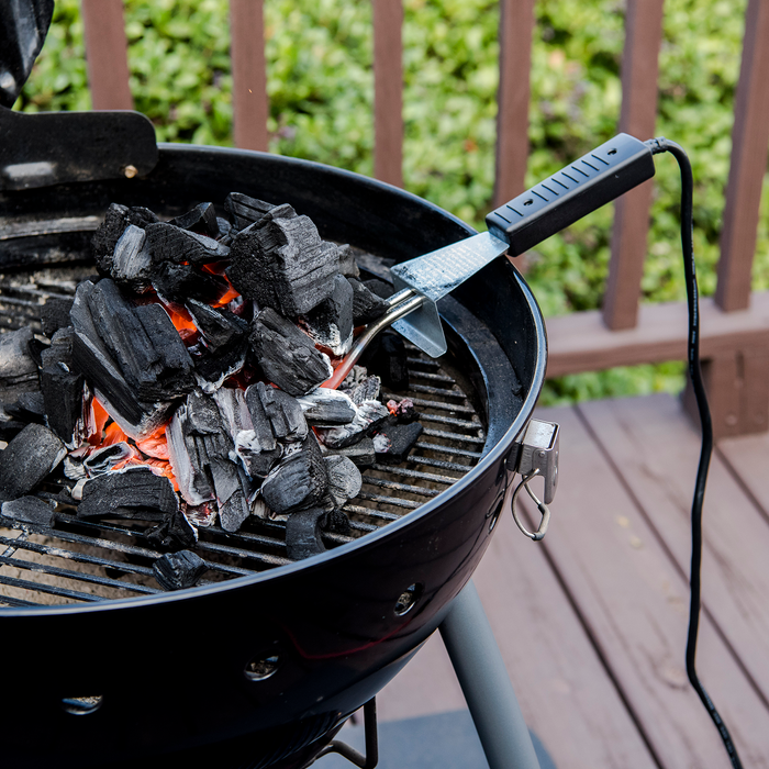 Black charcoal grill with glowing coals and metal tool.
