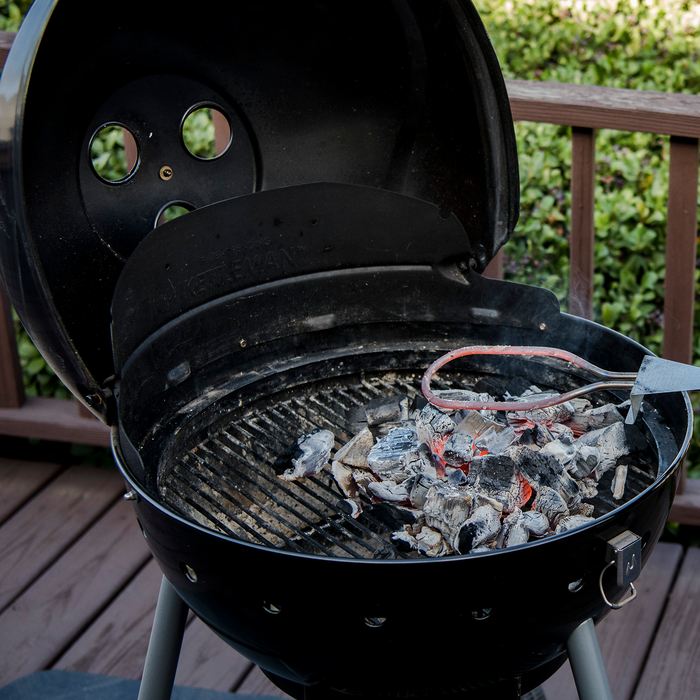 Black Weber kettle grill with charcoal and red-handled tongs.