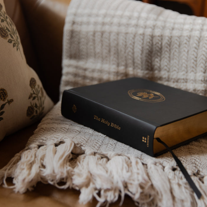 Black Bible on a textured surface with pillows and a blanket in the background