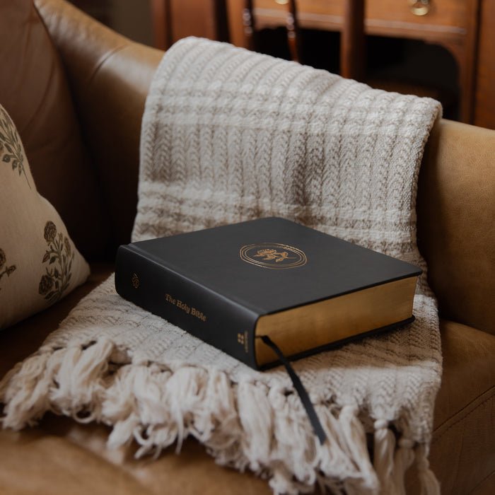 Black bible with gold embossed design on a beige couch with a textured blanket